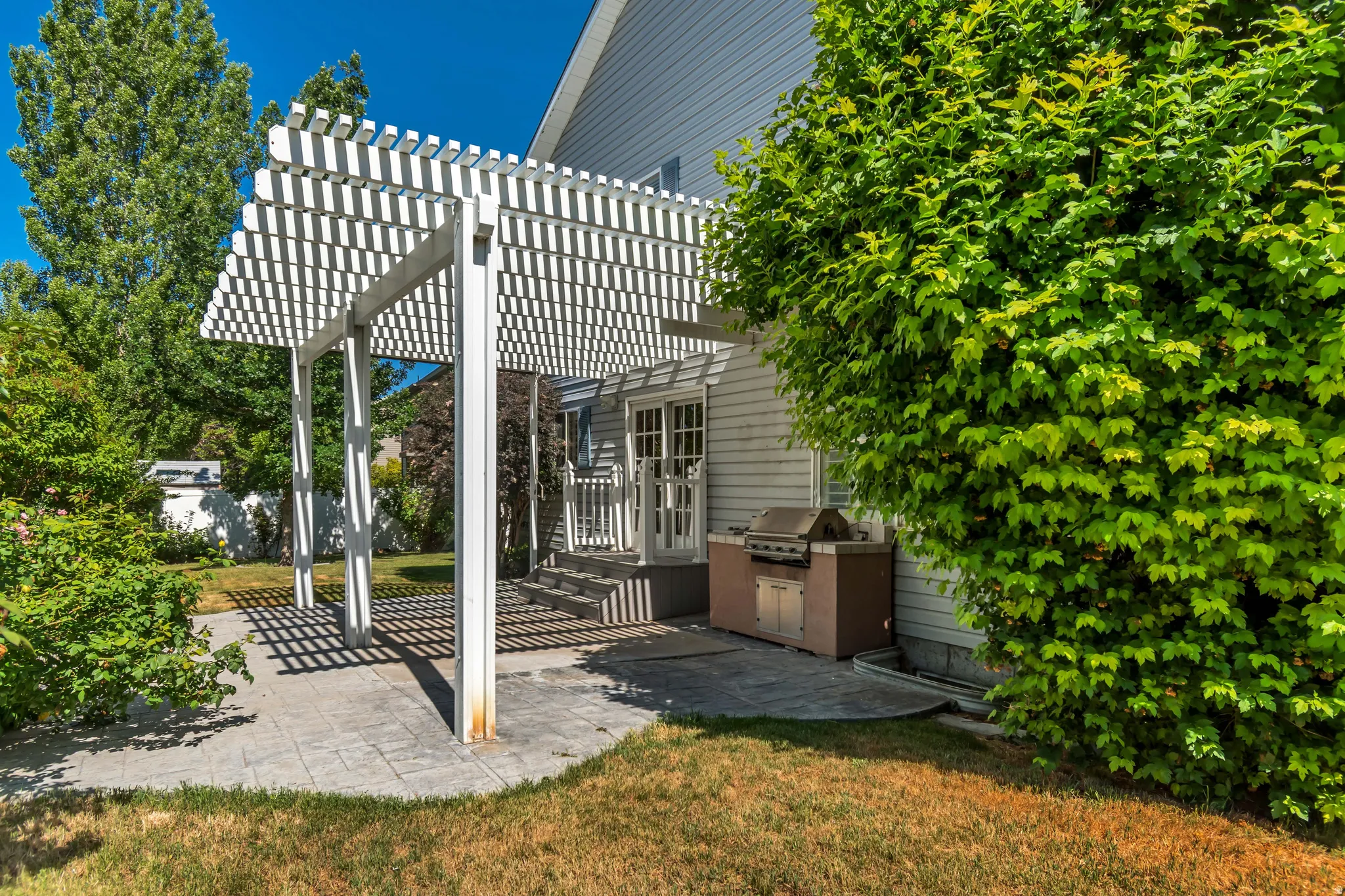 Exterior patio featuring a white pergola structure over stamped concrete pavers w/ barbeque