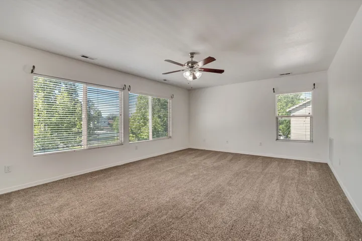 Spacious Master bedroom, featuring carpeting, multiple windows with blinds, a ceiling fan with integrated lighting, and neutral wall tones