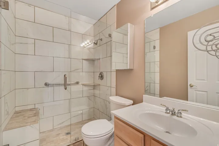 Spacious bathroom featuring a glass-enclosed shower with white tiled walls, an integrated shower bench, and a built-in shelf