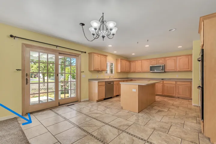 Kitchen featuring extensive light wood cabinetry, a central island, stainless steel appliances, and custom tile (blue arrow) with decorative inlay