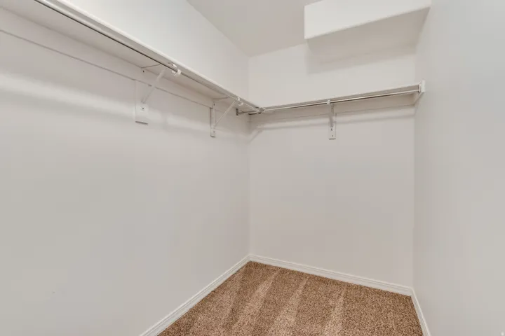 3rd Bedroom walk-in closet featuring light brown carpeting, white walls, and built-in white wire shelving with hanging rods