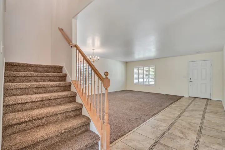 Entryway featuring tiled flooring with decorative inlays, a white paneled front door, and a carpeted staircase with a wood railing