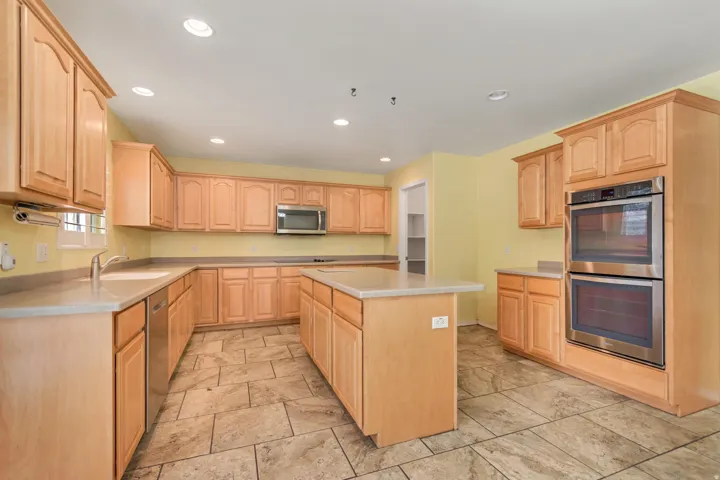 Kitchen featuring Corian countertops central island, stainless steel appliances including a double oven and built-in microwave, and tile flooring