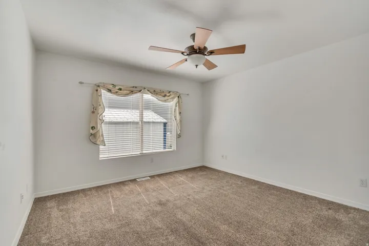 Carpeted room featuring a ceiling fan with light fixture, window with blinds, and white painted walls