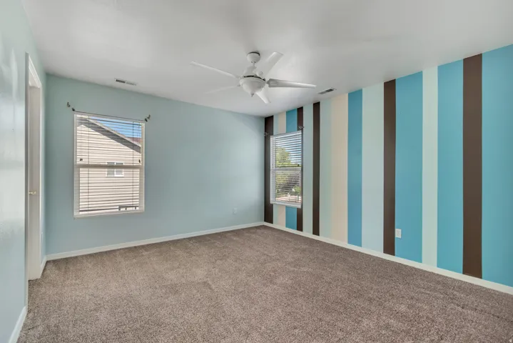 2nd Bedroom featuring a ceiling fan, two windows with blinds, light blue walls, and a prominent accent wall