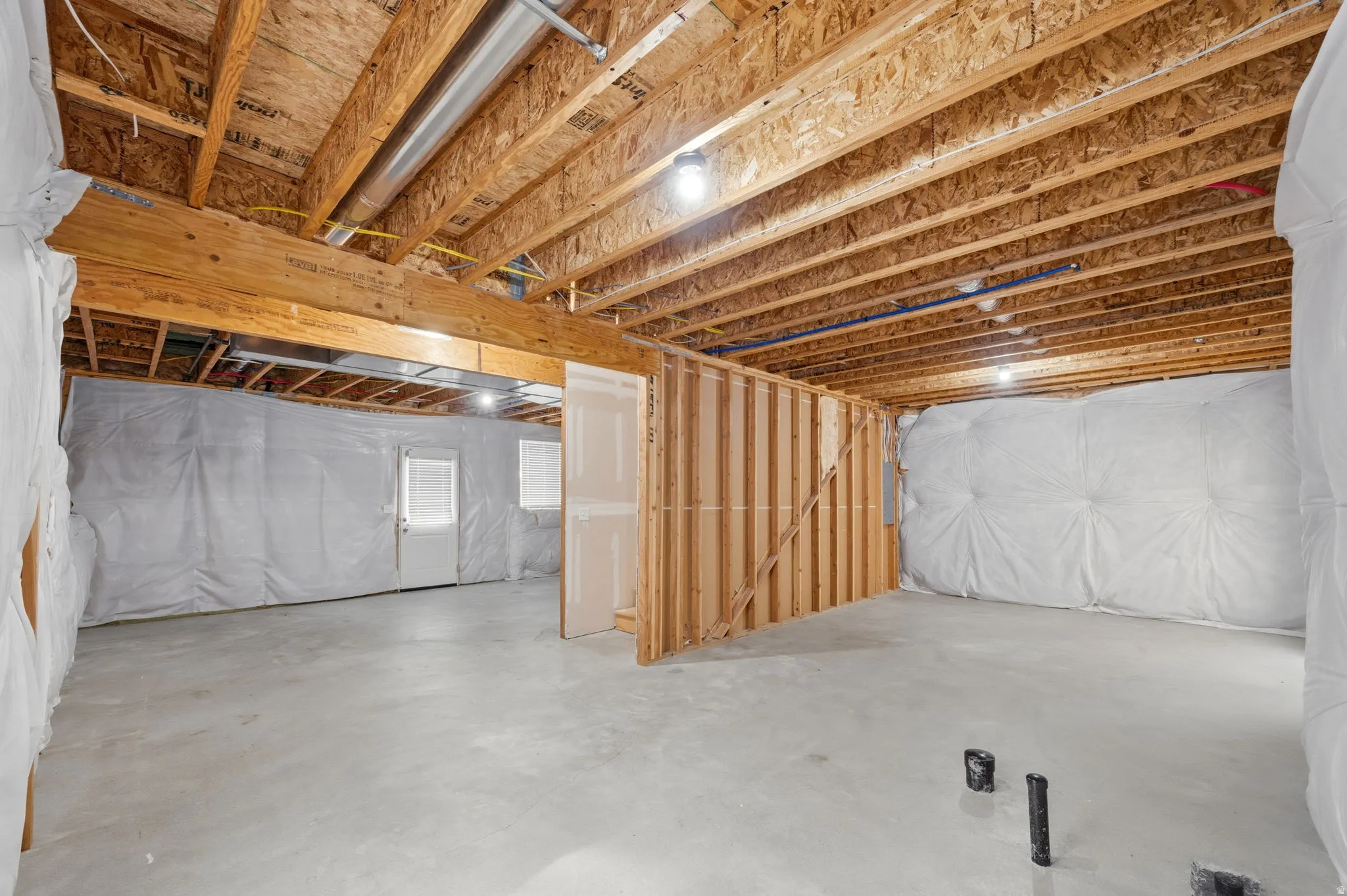 Unfinished basement featuring concrete flooring, framed interior walls, basement walkout and rough plumbing.
