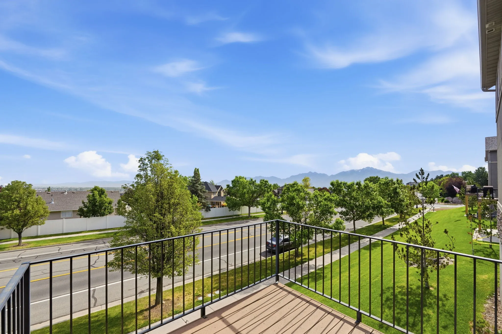 Balcony with wood-finish decking and black metal railing overlooking a landscaped street with distant mountain scenery