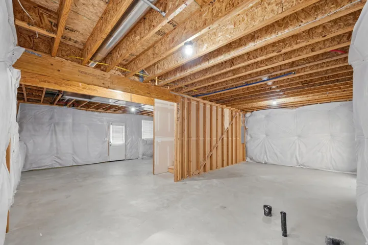 Unfinished basement featuring concrete flooring, framed interior walls, basement walkout and rough plumbing.