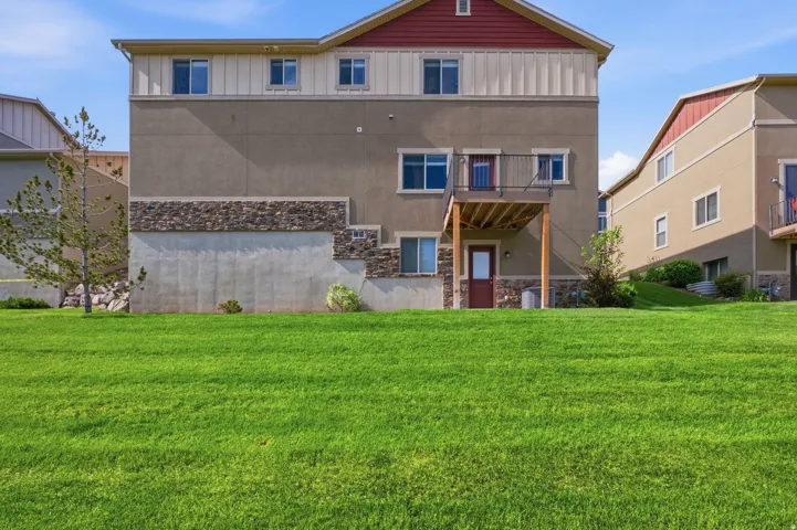 Expansive grassy backyard featuring a multi-level exterior, stone accents, upper-level balcony, and lower-level patio access