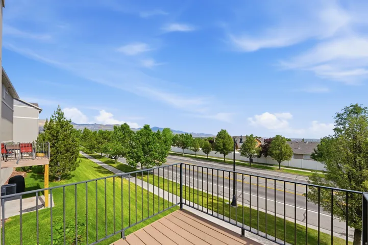 Private balcony with composite decking and black metal railing, featuring a landscaped greenbelt and a street with mature trees