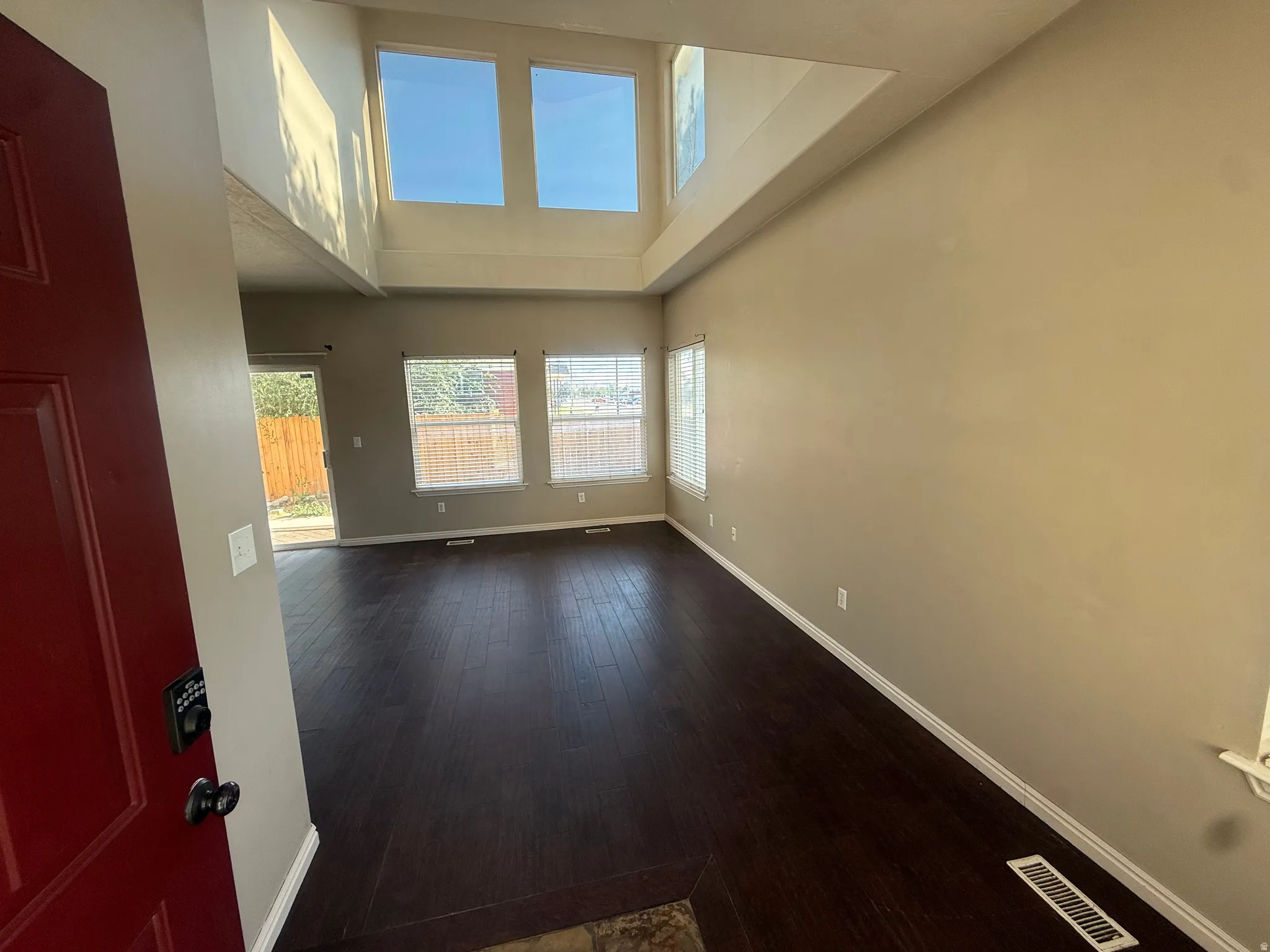 Vaulted ceiling with high windows, dark wood-finish flooring, multiple windows with blinds, and neutral wall paint