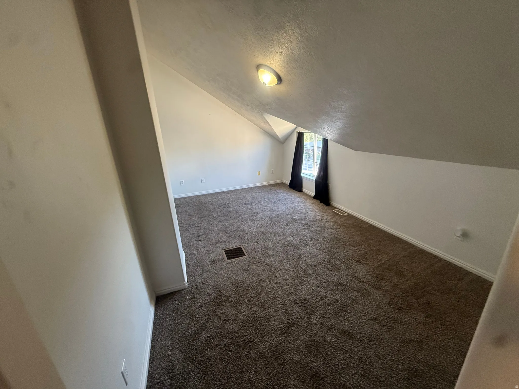Carpeted room with sloped ceilings and a flush-mounted ceiling light fixture