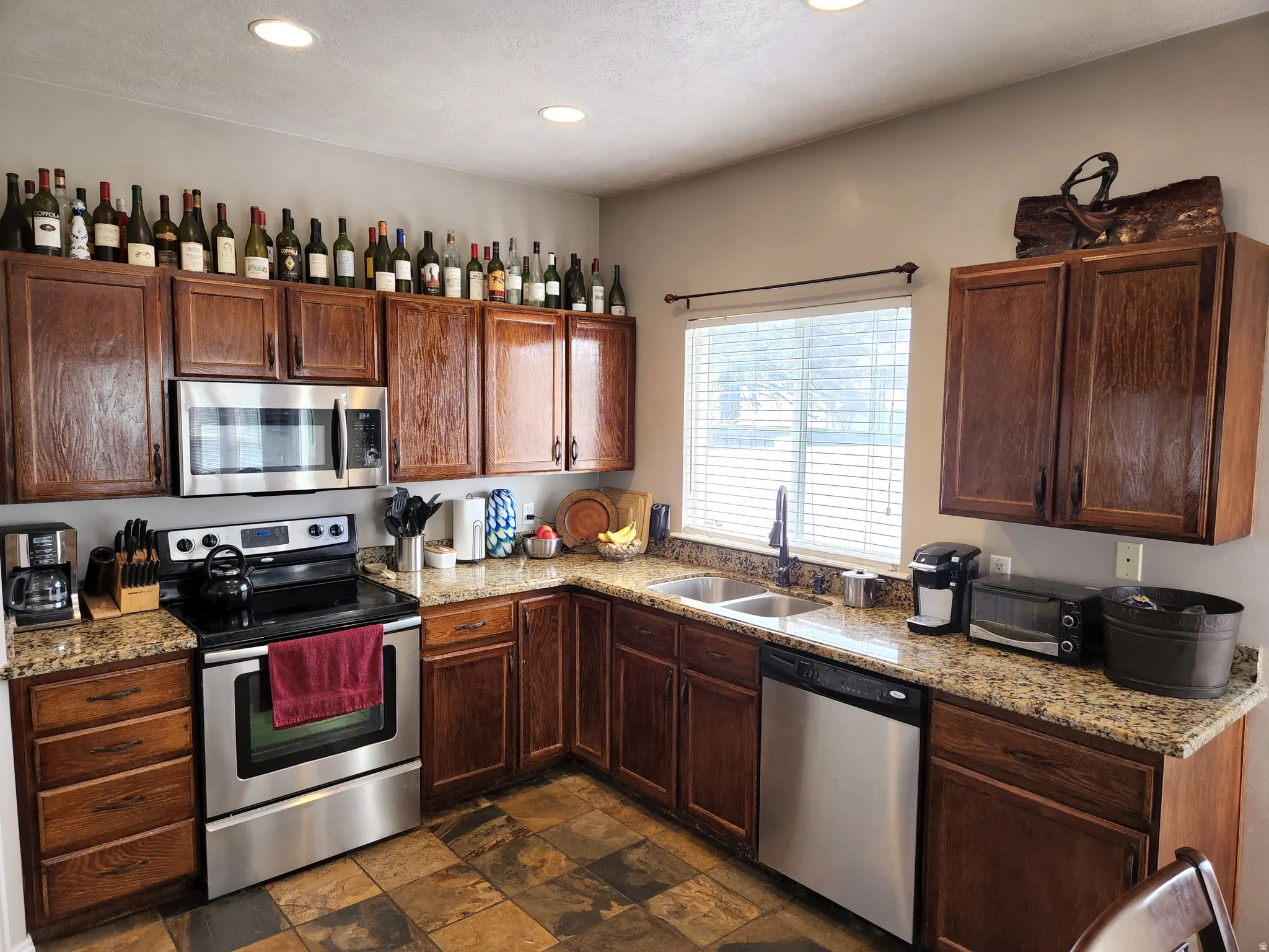 Kitchen featuring wood cabinetry, stainless steel appliances, granite countertops, a double basin sink, Slate tile flooring, and recessed lighting