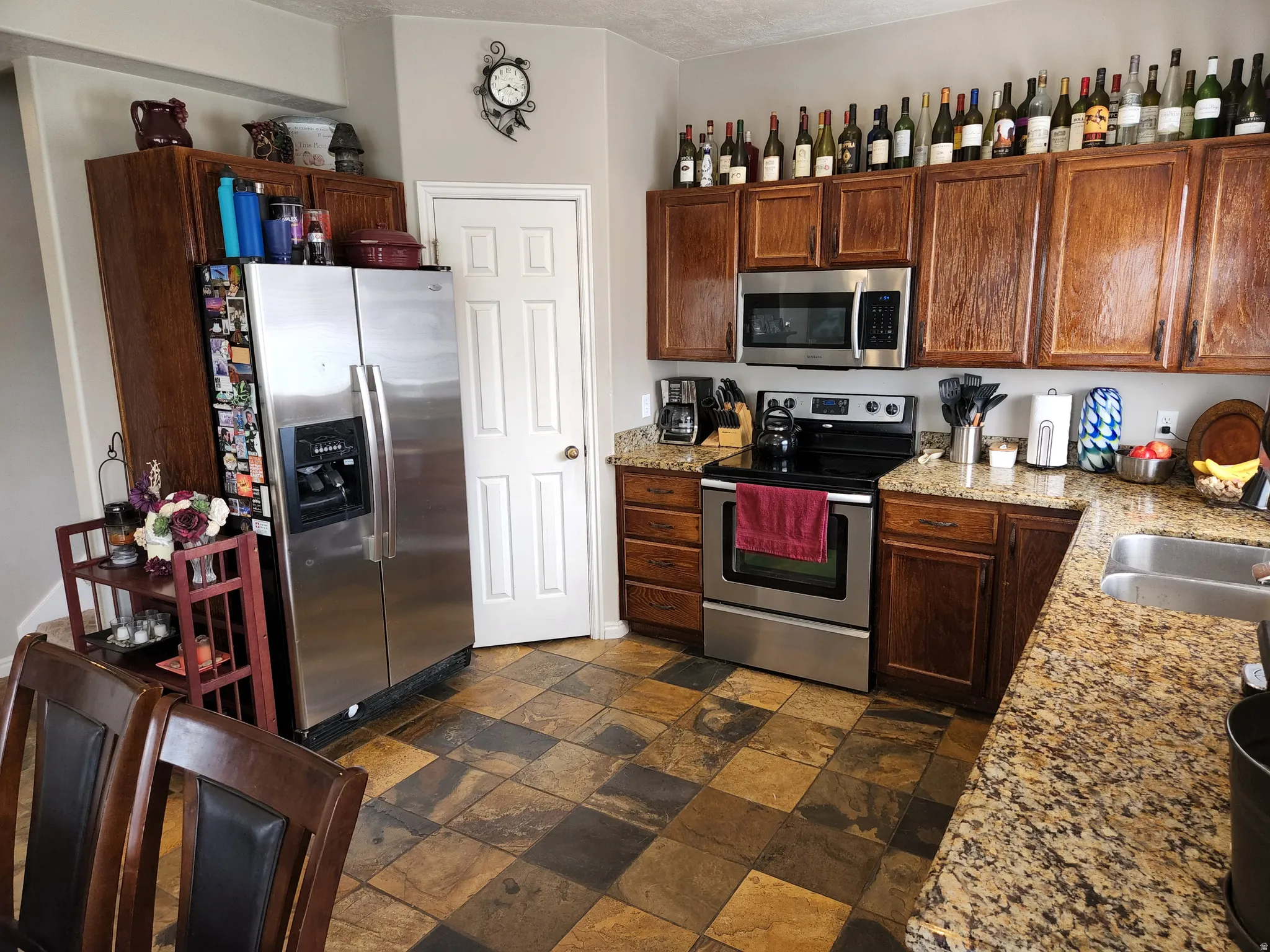 Kitchen featuring rich wood cabinetry, stainless steel appliances, speckled stone quartz countertops, a pantry, and multi-toned square floor slate tiles