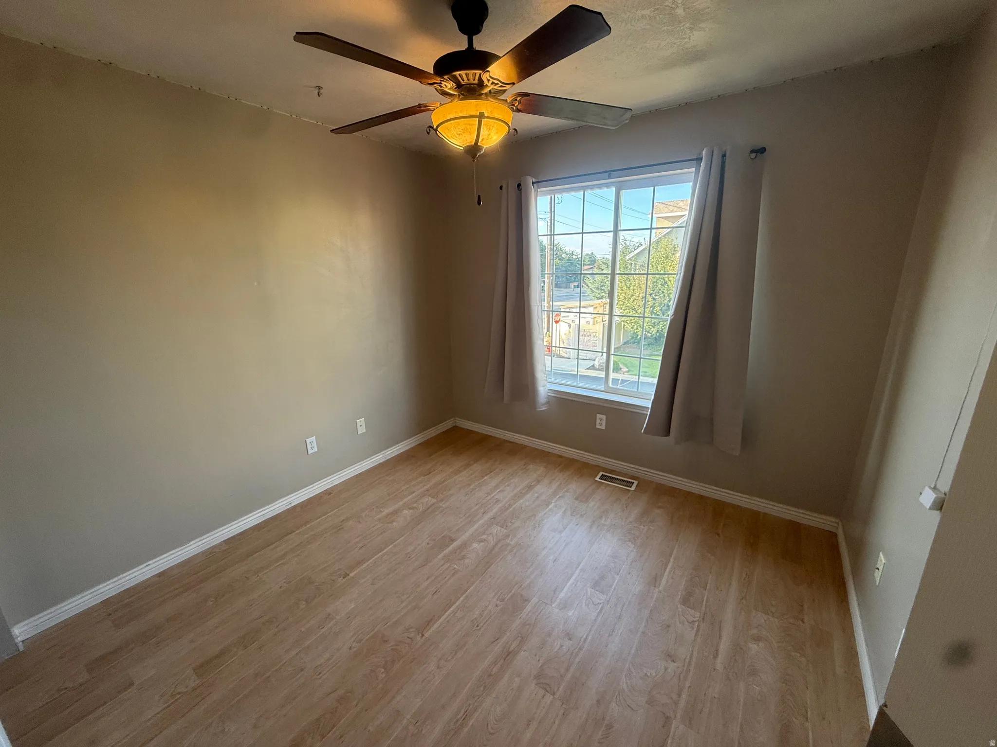 Wood-finish flooring with a ceiling fan light fixture and a single window