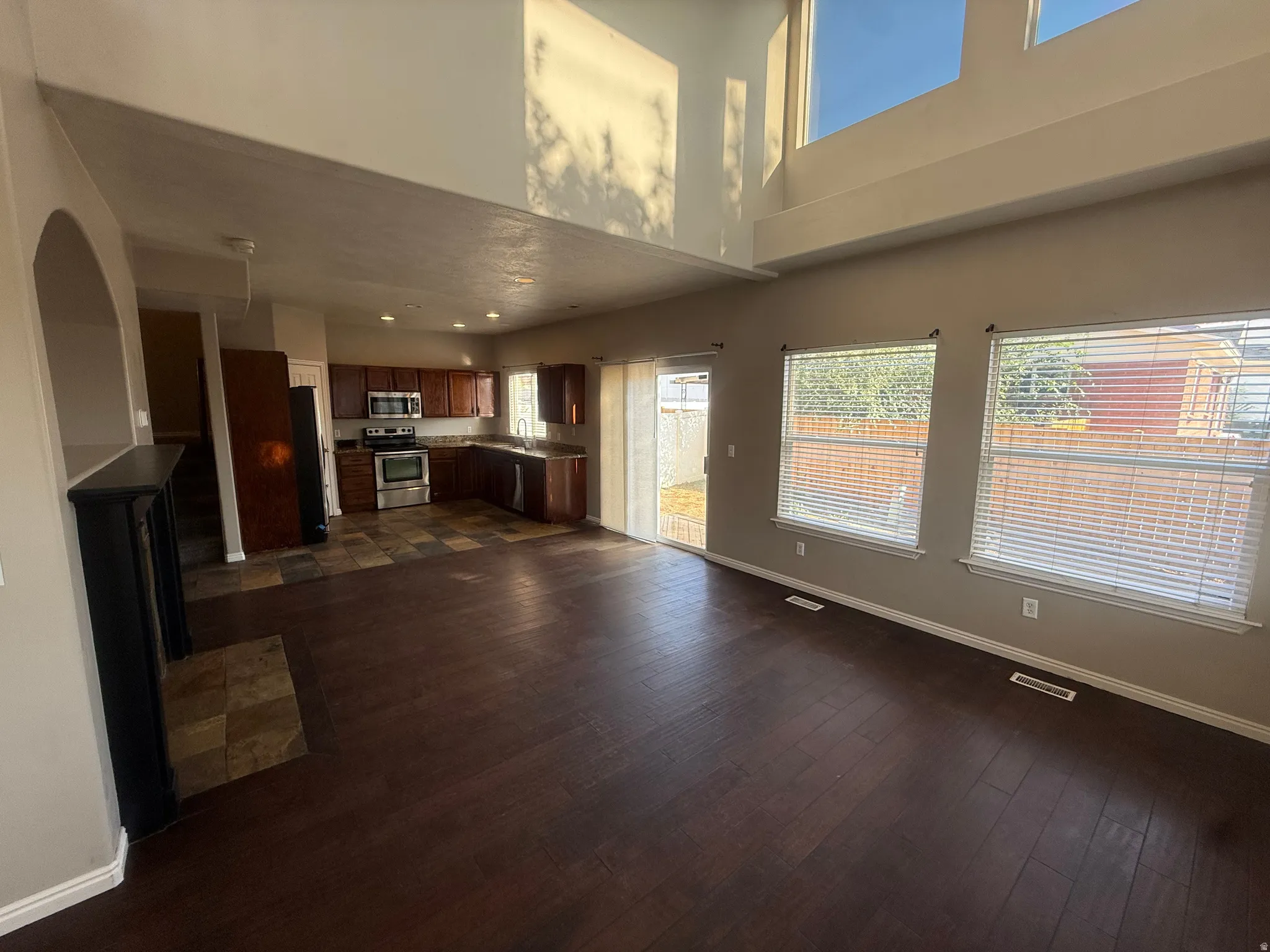 Two-story ceilings with upper windows, dark wood-finish flooring, and a kitchen featuring dark cabinetry with stainless steel appliances