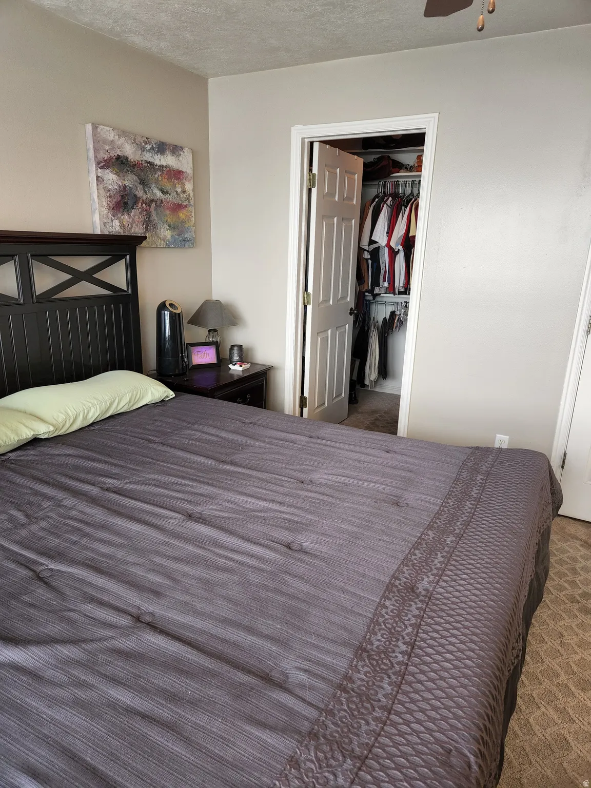 Master bedroom featuring light neutral wall paint, a ceiling fan, walk in closet, and carpet flooring
