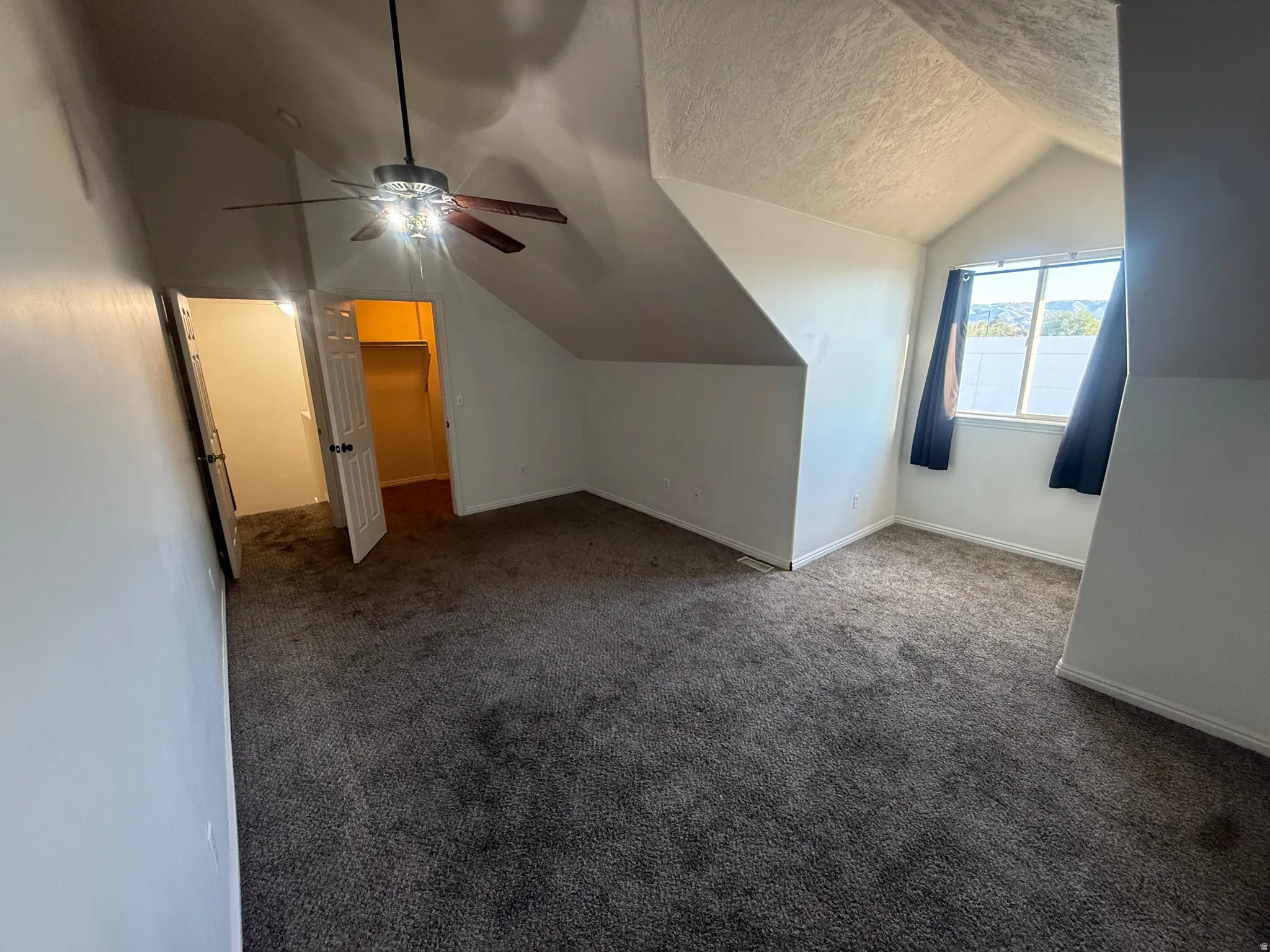 Sloped ceilings with a ceiling fan, carpeted flooring, and a window with a valance
