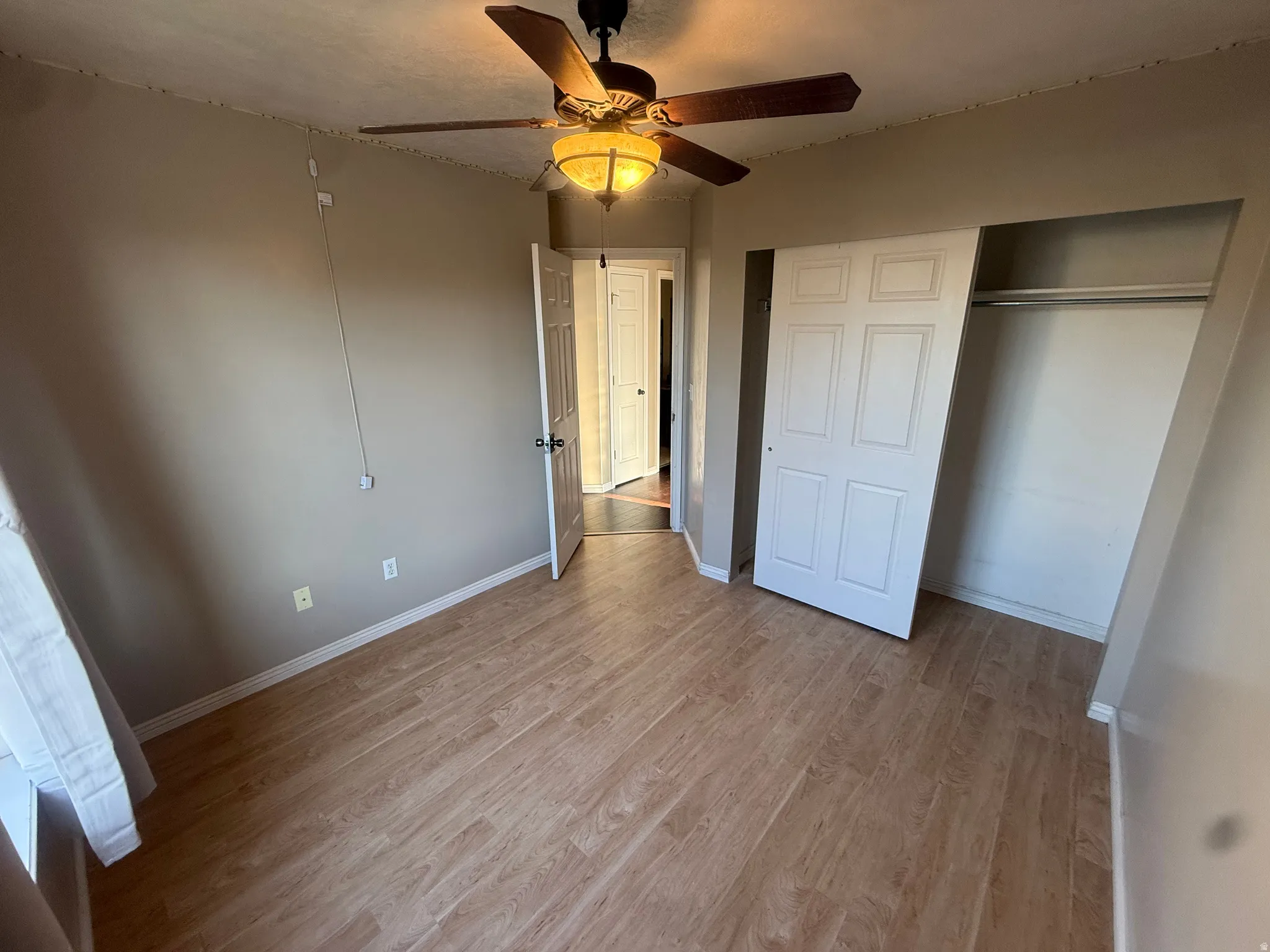 Wood-finish flooring throughout, featuring a ceiling fan with integrated lighting, and a closet with sliding panel doors