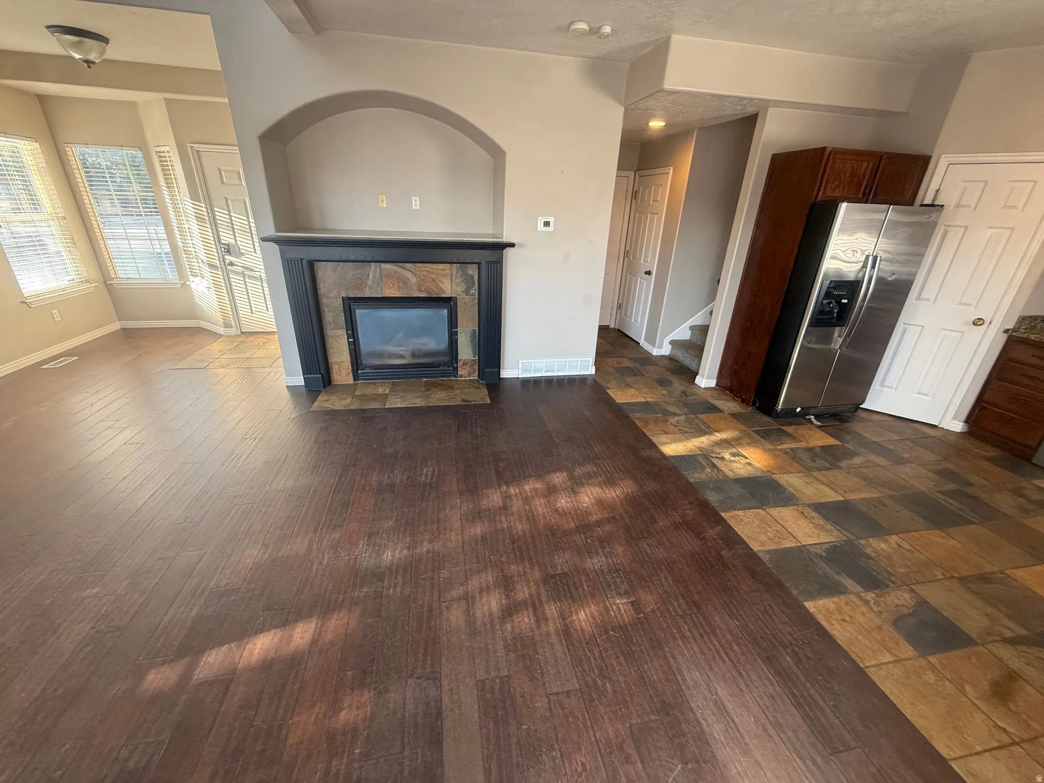 Wood-finish flooring, tiled fireplace surround, built-in fireplace, arched wall niche, and natural stone flooring