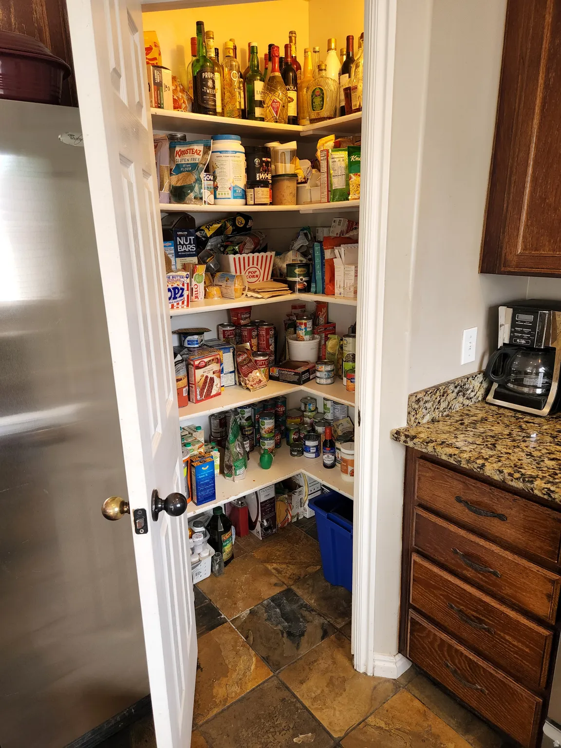 Corner pantry with built-in shelving, slate tile flooring, and a solid white door