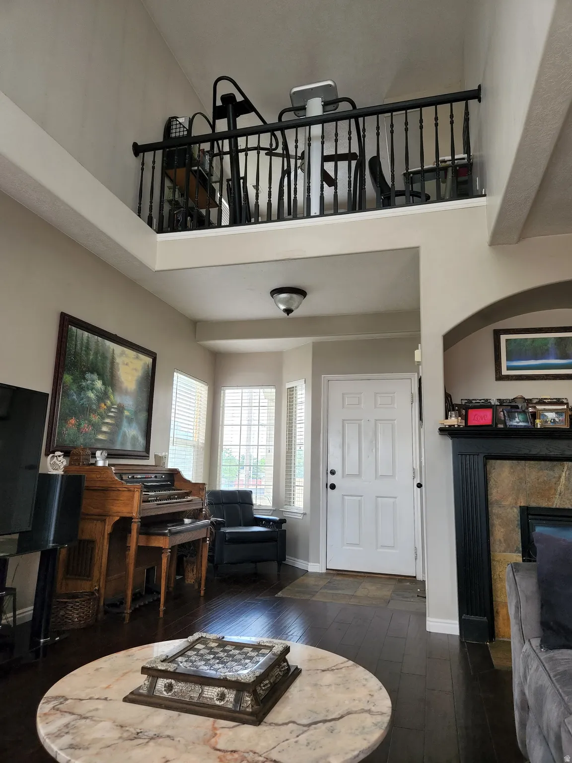 View of front entry. Two-story living area featuring a prominent loft with black baluster railing, dark wood-finish flooring, and a multi-pane bay window