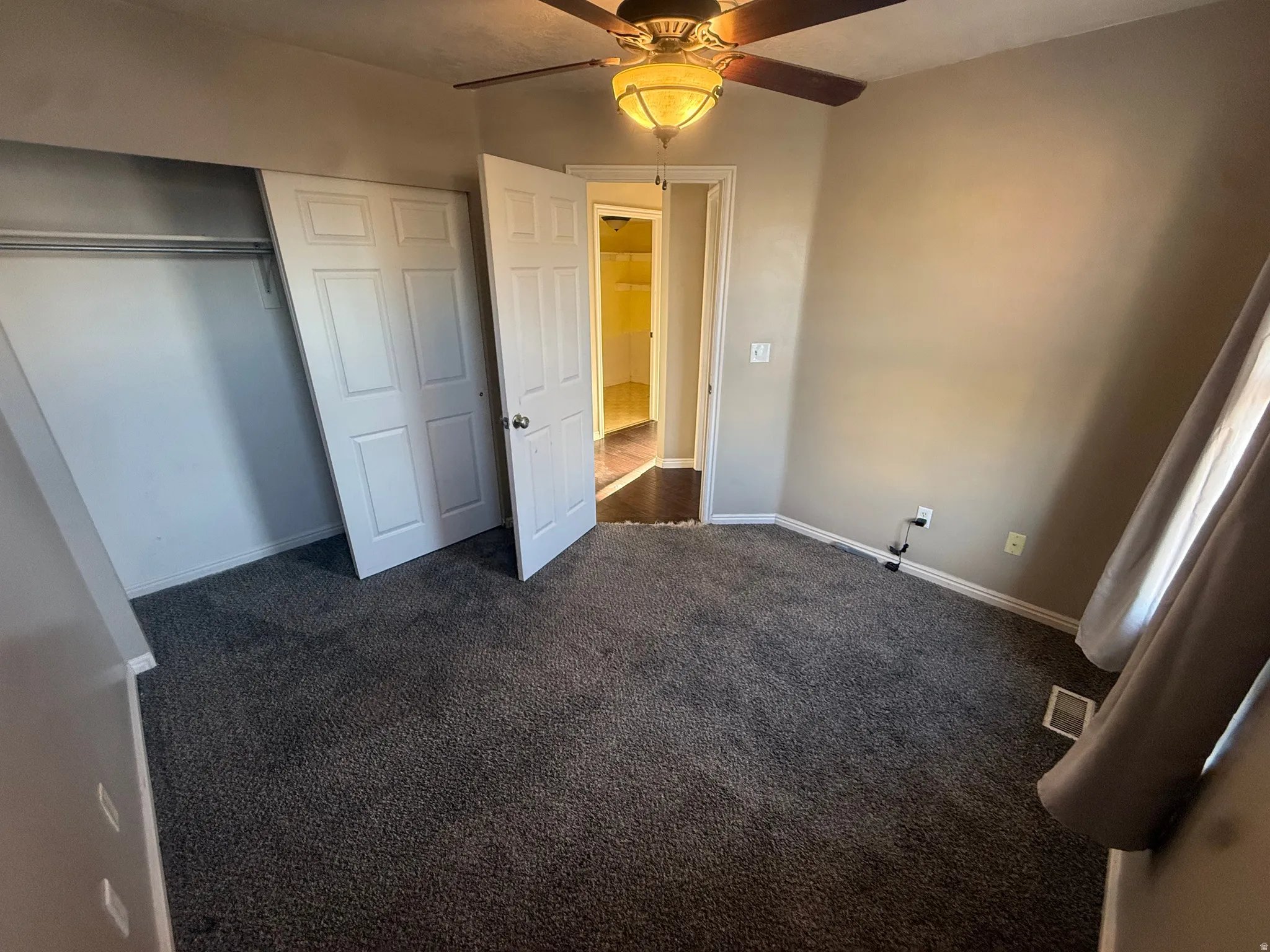 Built-in closet with bi-fold doors, overhead ceiling fan with light fixture, wall-to-wall carpeting