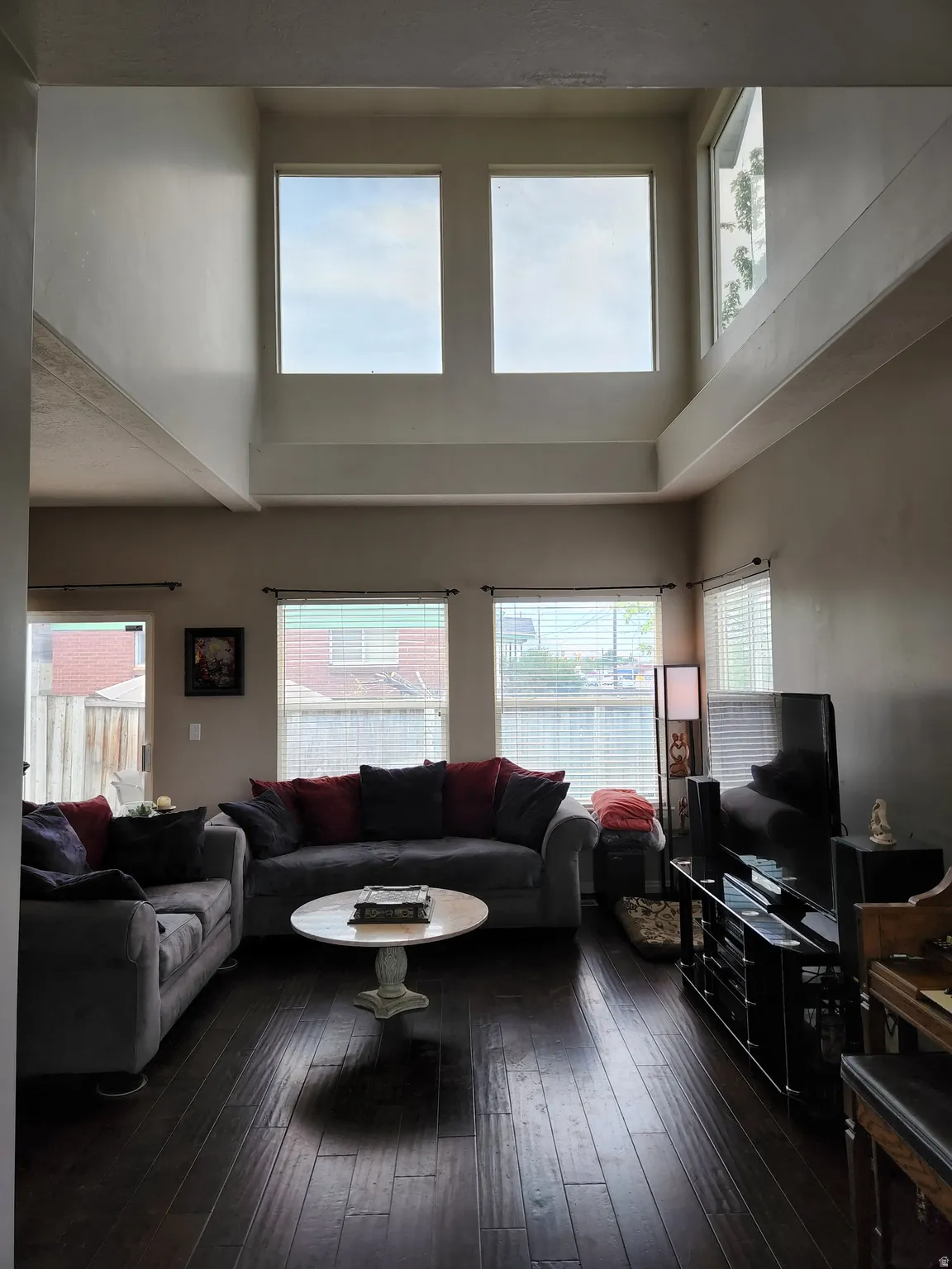 View from entry. Open-concept living space with dark wood-finish flooring, high ceilings, multiple windows, and a glass-paned door