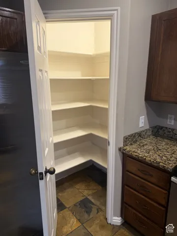 Walk-in pantry with multiple corner shelves, slate tile flooring, and a paneled door with bronze hardware