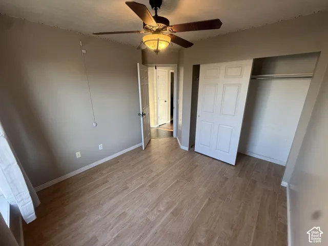 Wood-finish flooring throughout, featuring a ceiling fan with integrated lighting, and a closet with sliding panel doors