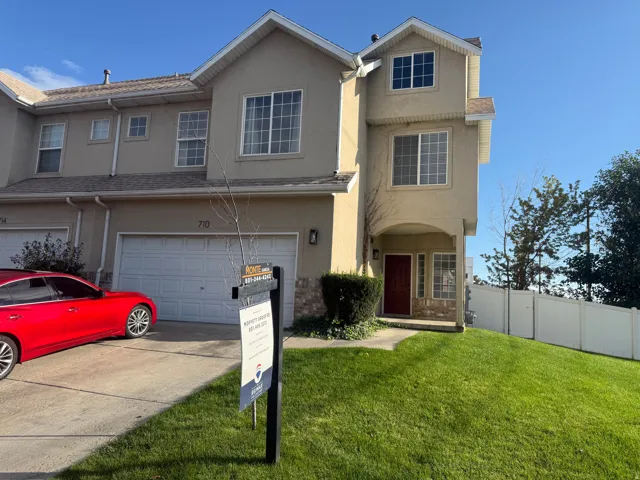 Stucco exterior with multiple windows, an attached two-car garage, a red entry door, and a manicured lawn