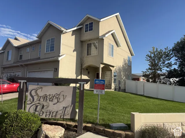 Stucco exterior, multi-level design, attached garage, gabled roofline, and landscaped front yard