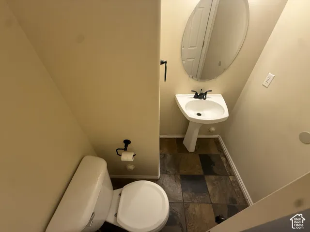 Pedestal sink with dark-toned fixtures, oval wall mirror, and multi-toned tile flooring