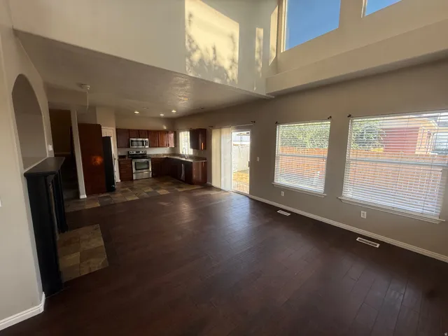 Two-story ceilings with upper windows, dark wood-finish flooring, and a kitchen featuring dark cabinetry with stainless steel appliances