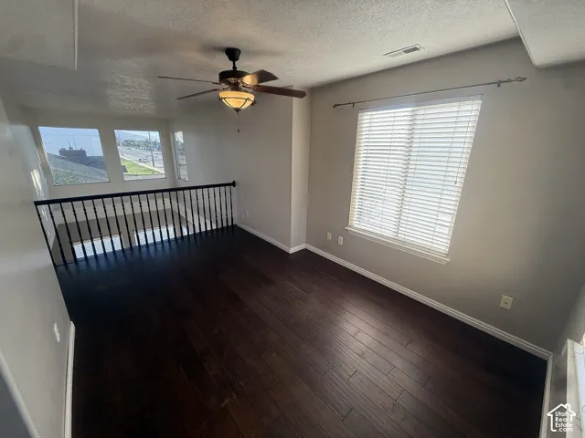 Dark wood-finish flooring, ceiling fan with integrated lighting, multiple windows with blinds, and wrought iron railing