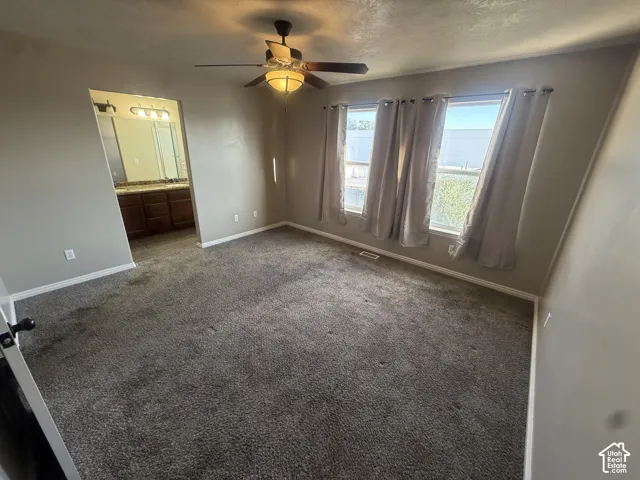 Carpeted room with multiple windows, a ceiling fan with integrated lighting, and an adjacent bathroom featuring a dual vanity with a countertop and under-cabinet storage