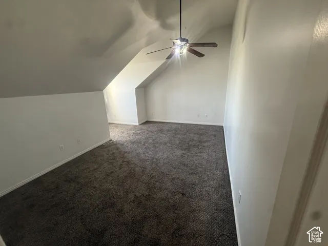 Spacious room with sloped ceilings, plush carpet flooring, a ceiling fan with integrated lighting, and neutral wall finishes