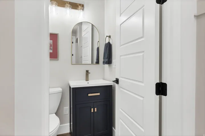 Powder room featuring a dark blue vanity with gold hardware, a white vessel sink, and a gold-finish faucet