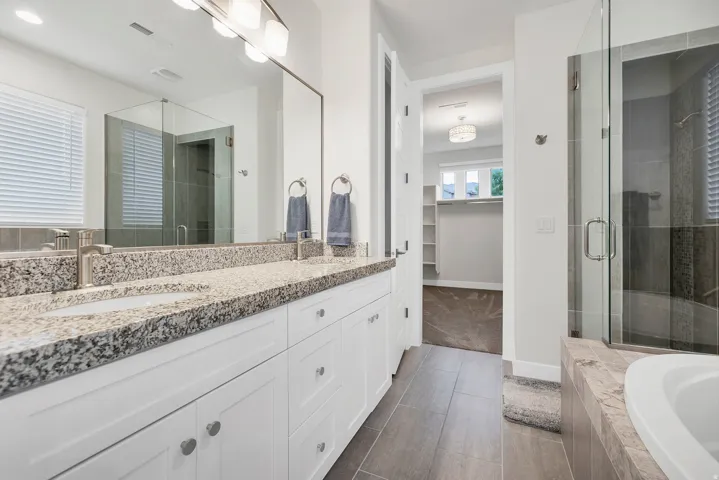 Spacious bathroom featuring a dual vanity with granite-finish countertop, white cabinetry, and brushed nickel fixtures