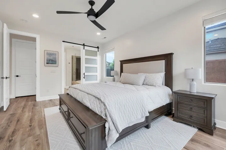 Spacious bedroom featuring wood-finish flooring, a modern black ceiling fan, recessed lighting, and a barn door entry to an adjoining space