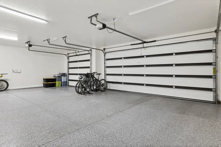 Two-car garage featuring a speckled epoxy floor coating, two white sectional garage doors with black accents, automatic garage door openers, and fluorescent overhead lighting