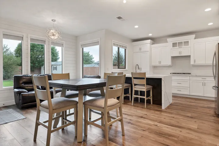 Open-concept kitchen and dining area featuring wood-finish flooring, white cabinetry with silver hardware, a waterfall island, and multiple windows