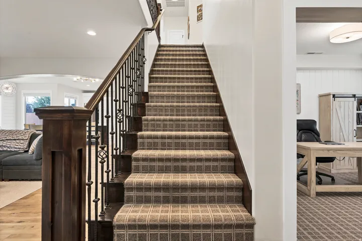 Carpeted staircase with an ornamental wrought iron and wood baluster system, a substantial newel post, and recessed lighting
