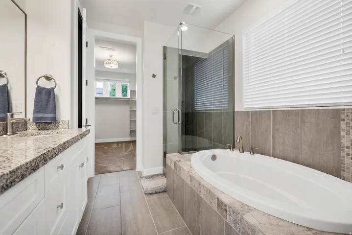 Contemporary bathroom featuring a freestanding soaking tub with deck-mounted fixtures, a glass-enclosed shower, and a double vanity with a stone-finish countertop