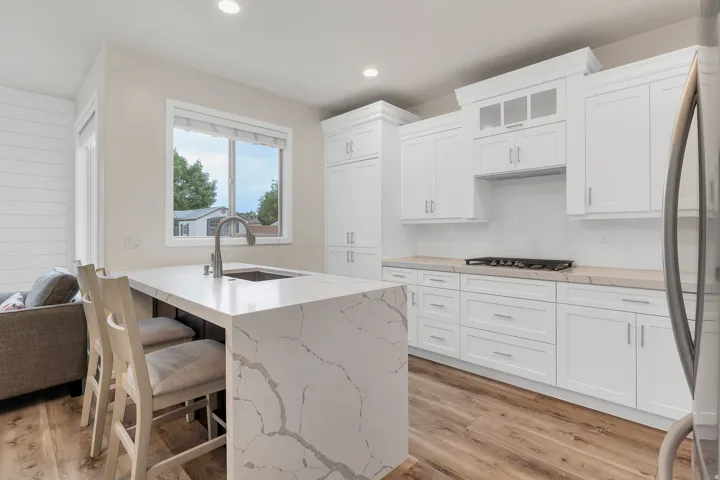 Kitchen featuring a waterfall island with a stainless steel sink, white shaker-style cabinetry, subway tile backsplash, a built-in gas range, and wood-finish flooring