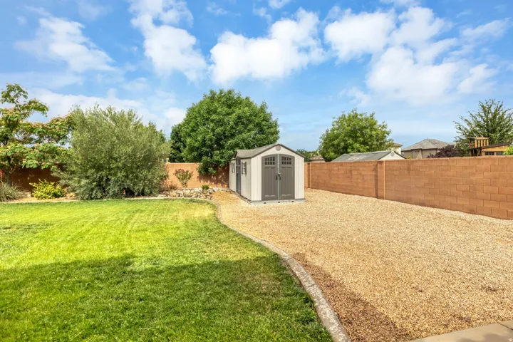 Expansive backyard featuring a manicured lawn, gravel hardscaping, mature trees, and a utility shed