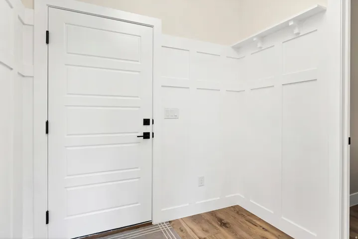 Entryway featuring a white paneled door with black hardware, complementing board and batten wall detailing, a built-in coat rack, and wood-finish flooring
