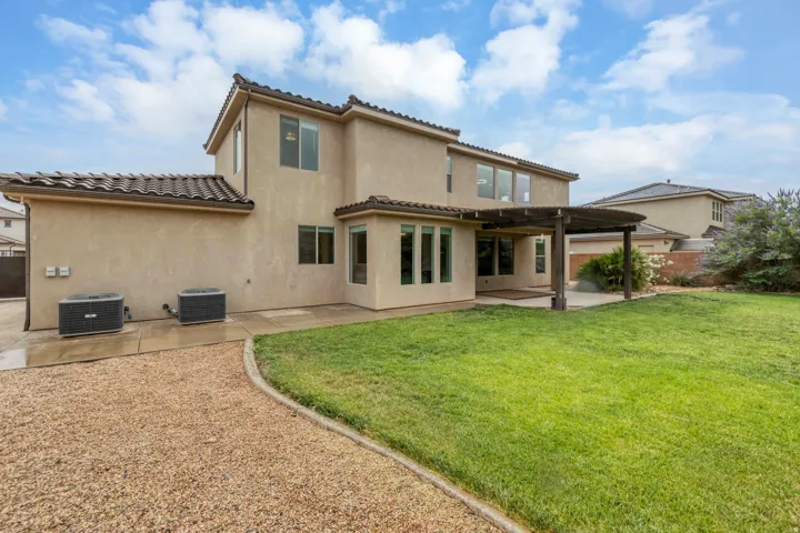 Expansive backyard featuring a manicured lawn, a gravel pathway, and a covered patio with a pergola structure