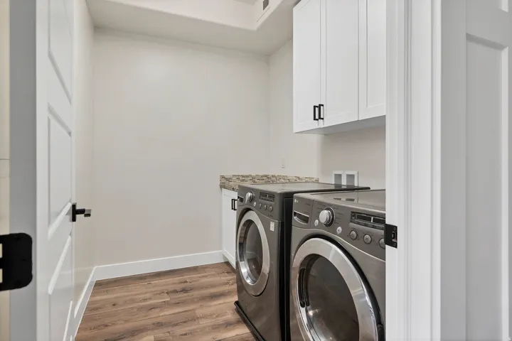 Laundry area featuring wood-finish flooring, white cabinetry with black hardware, a stone-finish countertop, and a white interior door with black hardware