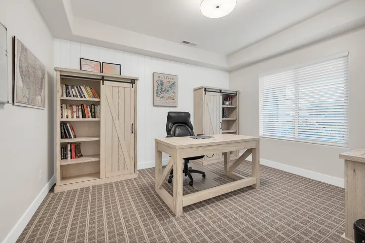 Spacious room featuring patterned carpet flooring, a large window with horizontal blinds, and a tray ceiling